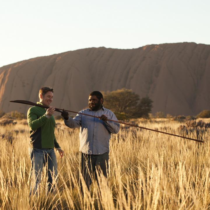 an indigenous man showing a tourist an atlatl